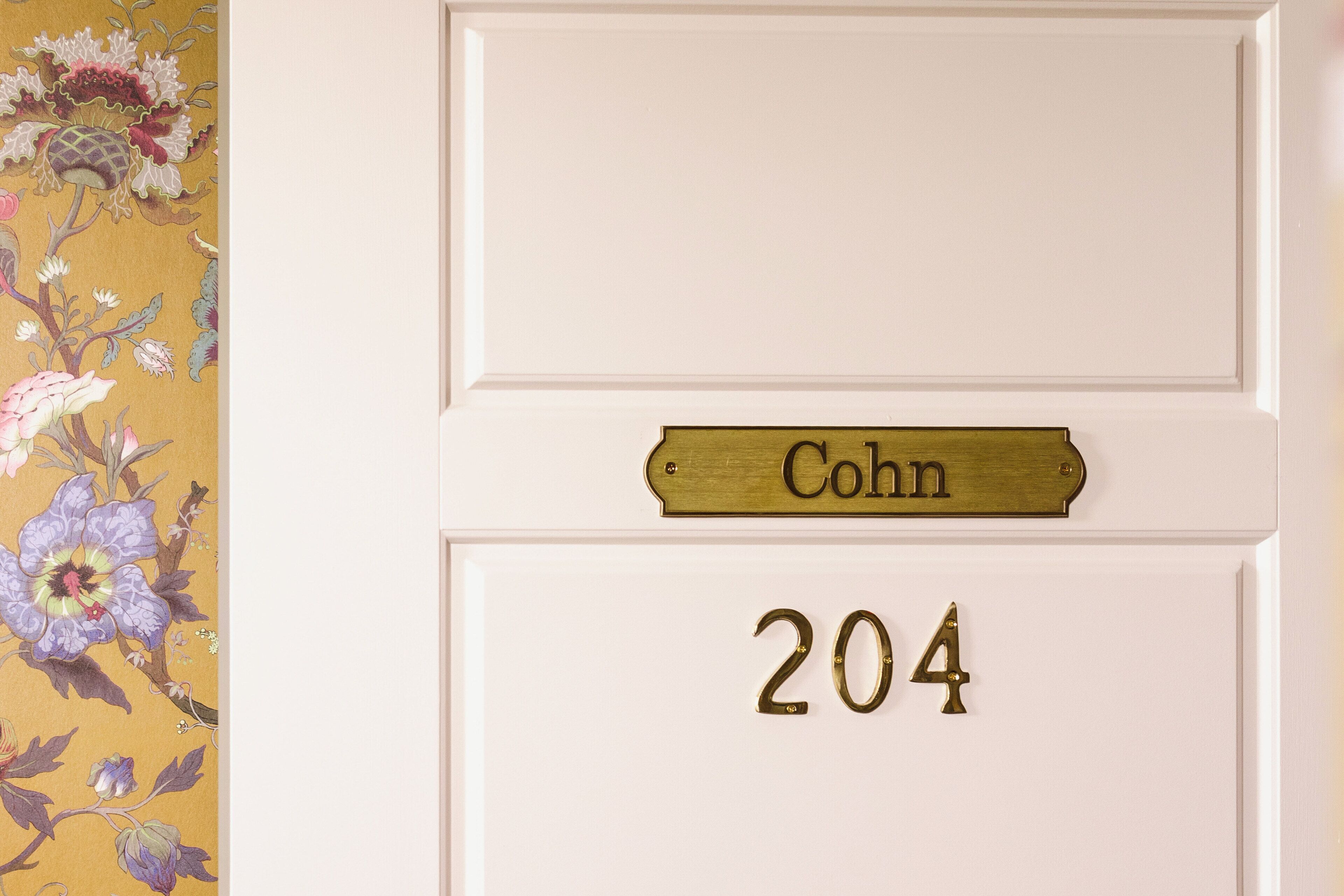 Ovi, jossa on messinkinen nimikyltti, jossa lukee ”Cohn”, ja messinkinen numero ”204” valkoisessa ovilevyssä.