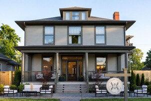 A two-story house with a front porch, a staircase leading to the entrance, and a sign indicating it is a boarding house.