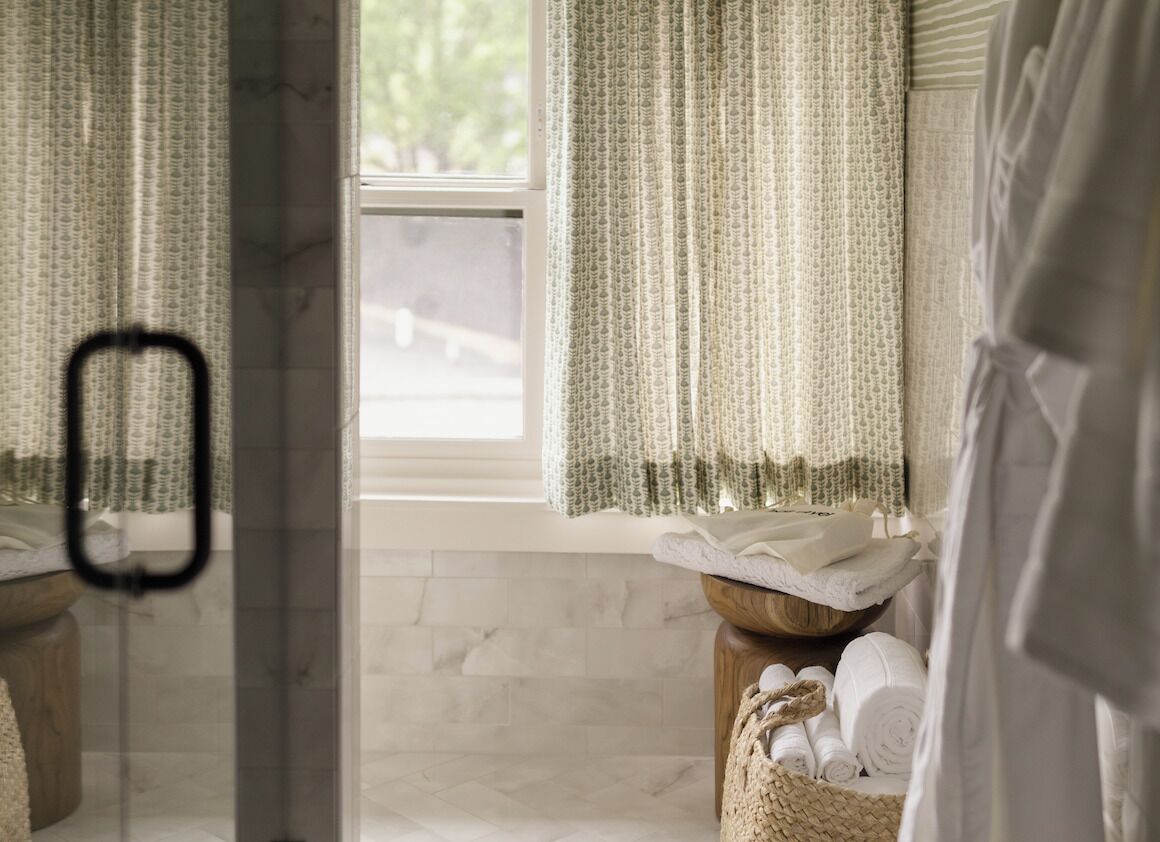 A bathroom with a window, a towel rack, and a wooden stool with towels.