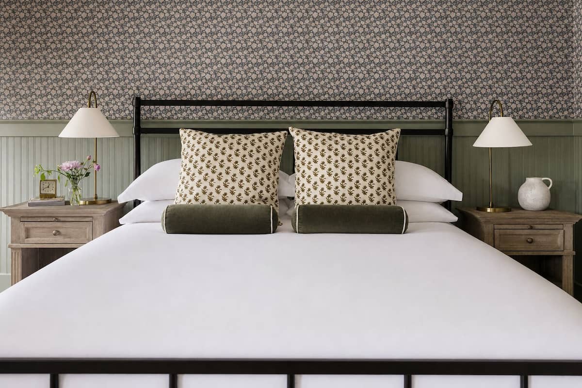 Una cama con cabecera, dos mesitas de noche con lámparas y un papel tapiz con estampado floral.