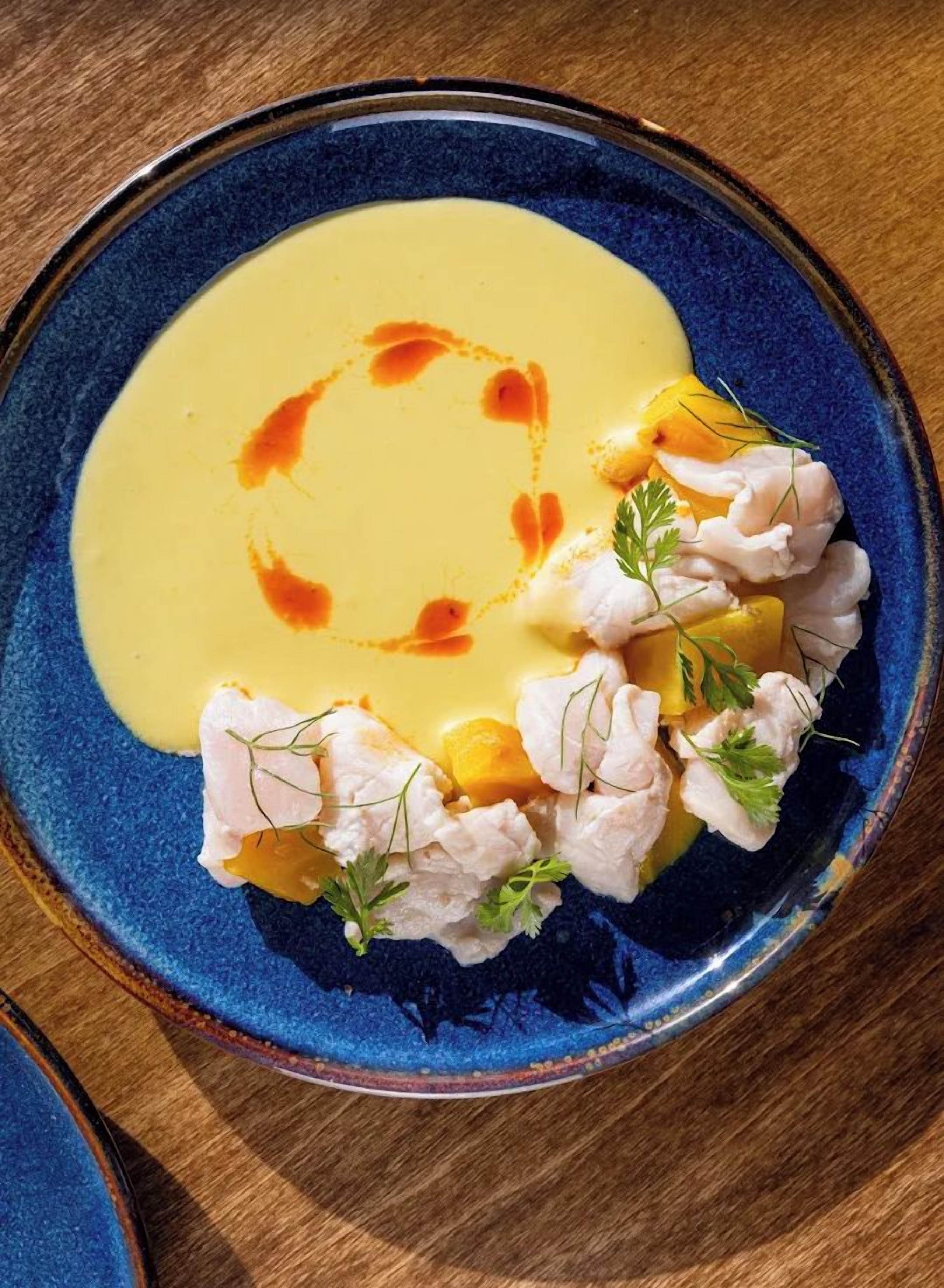 A plate of food with a blue rim, a yellow sauce, and garnished with herbs.