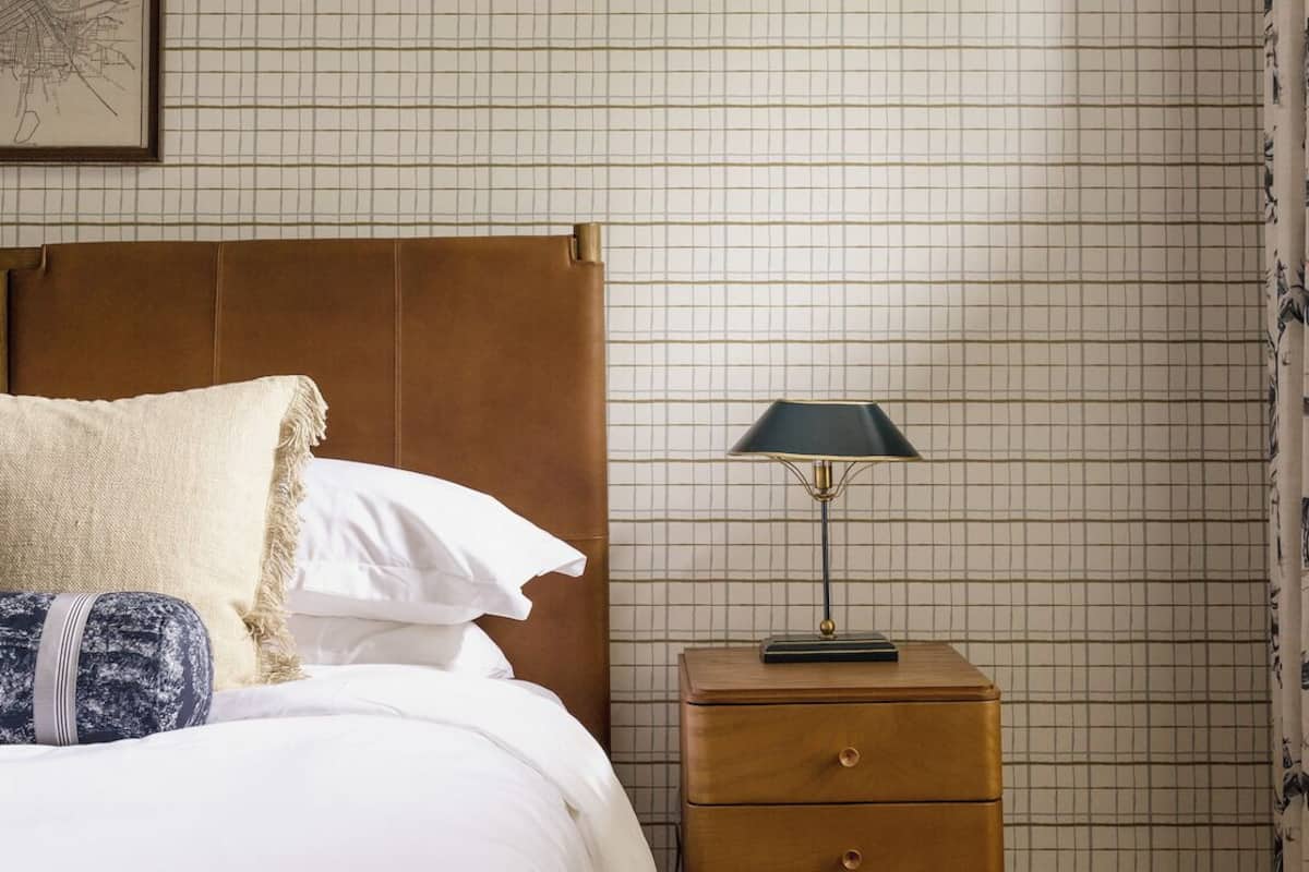 Una cama bien hecha con un cabecero marrón, una lámpara de noche y una mesita de noche de madera con cajones.