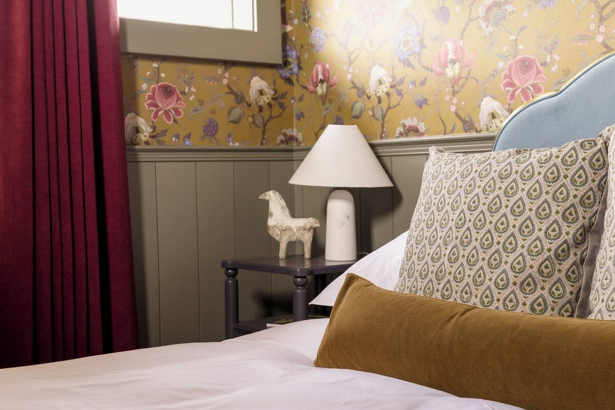 Un dormitorio con cama, mesita de noche, lámpara y papel tapiz con estampado floral.