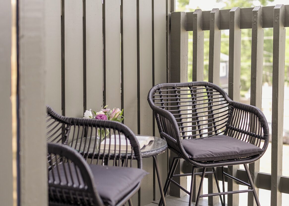 Two wicker chairs with cushions, a small round table, and a vase with flowers.