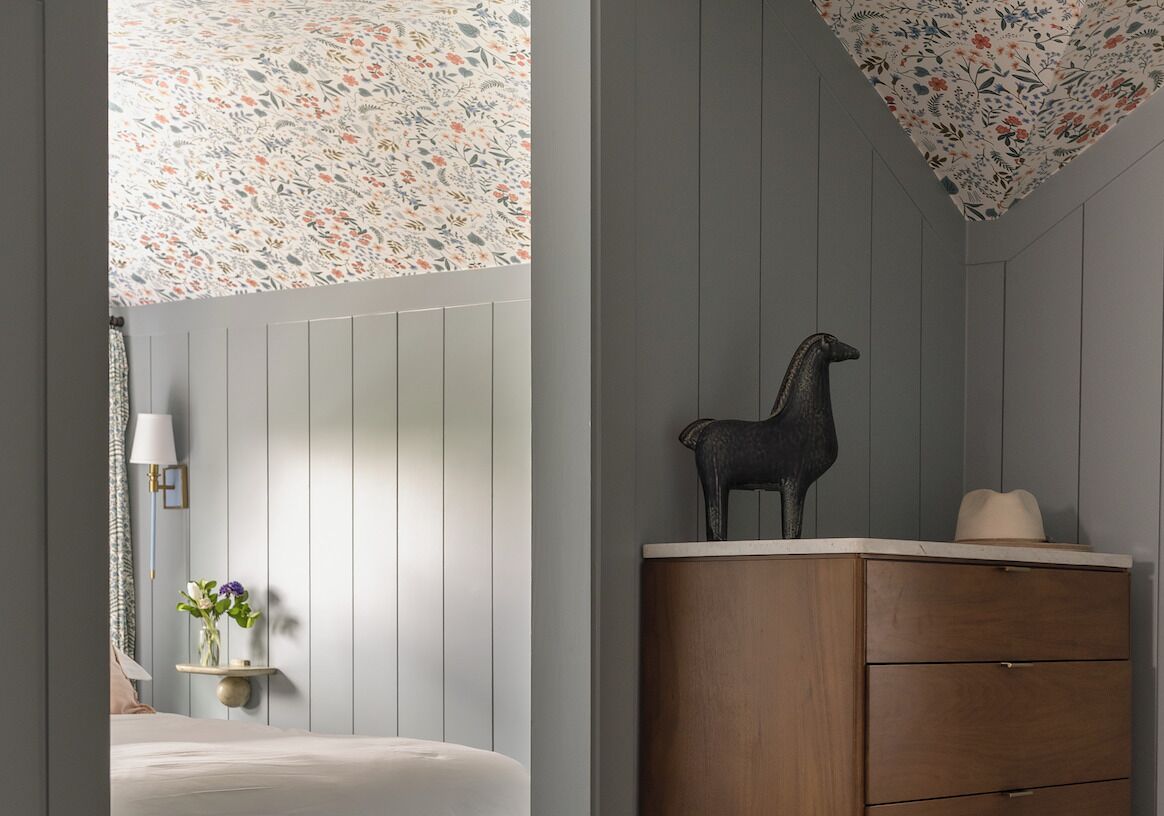 Un dormitorio con cama, cómoda, lámpara y techo estampado con motivos florales.