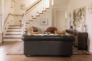 A living room with a dark leather sofa, a staircase, a console table with decorative items, and a large abstract painting on the wall.