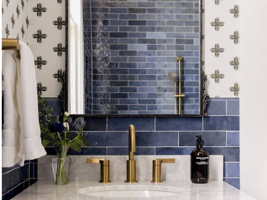 Een badkamer met een blauwe betegelde achterwand, een gouden kraan en een wit wastafel.