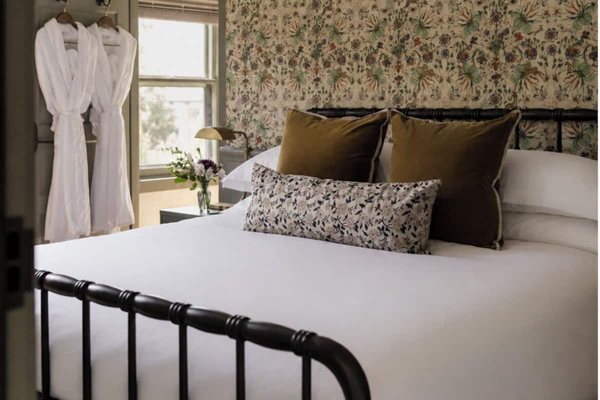 Un dormitorio con cama, papel tapiz floral y una ventana.