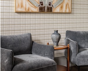 A room with a grey sofa, a small round table with a vase, and a grid-patterned wall. - Sylvan Park Boarding House  (Nashville)