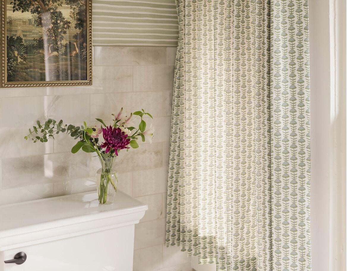A bathroom with a white sink, a vase with flowers, a framed picture on the wall, and a patterned shower curtain.