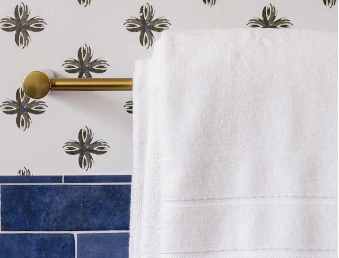A white towel hanging on a gold towel bar against a wall with a floral pattern.