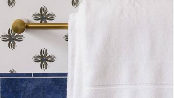 A white towel hanging on a gold towel bar against a wall with a floral pattern.