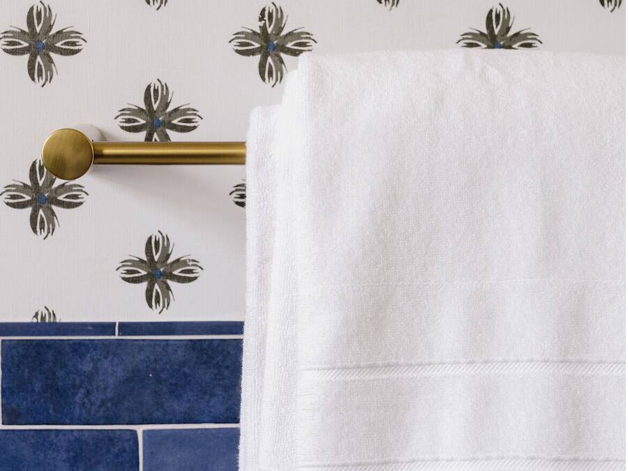 A white towel hanging on a gold towel bar against a wall with a floral pattern.