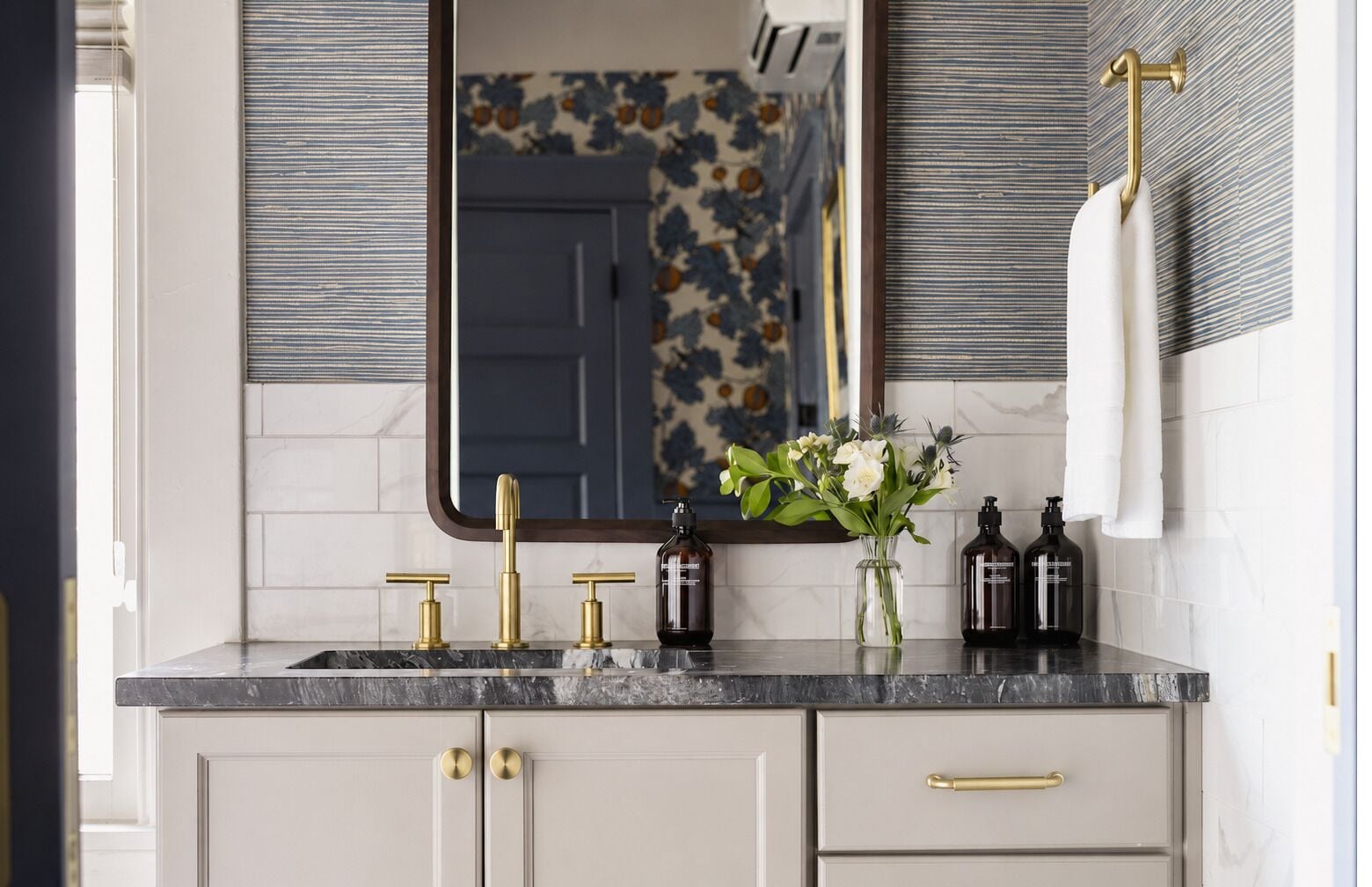 Um banheiro com bancada de mármore, torneiras douradas, espelho e um vaso com flores.