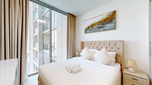 A hotel room with a large bed, a headboard, a nightstand with a lamp, and a painting on the wall.