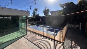 Ein Poolbereich auf dem Dach mit Glasveranda, Lichterketten und Blick auf Palmen.