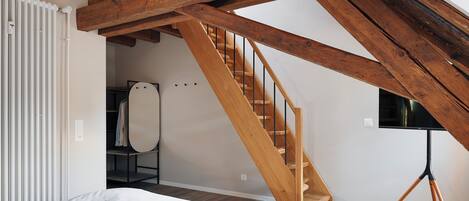 A bedroom with a wooden staircase, a bed, and a television on a tripod stand.