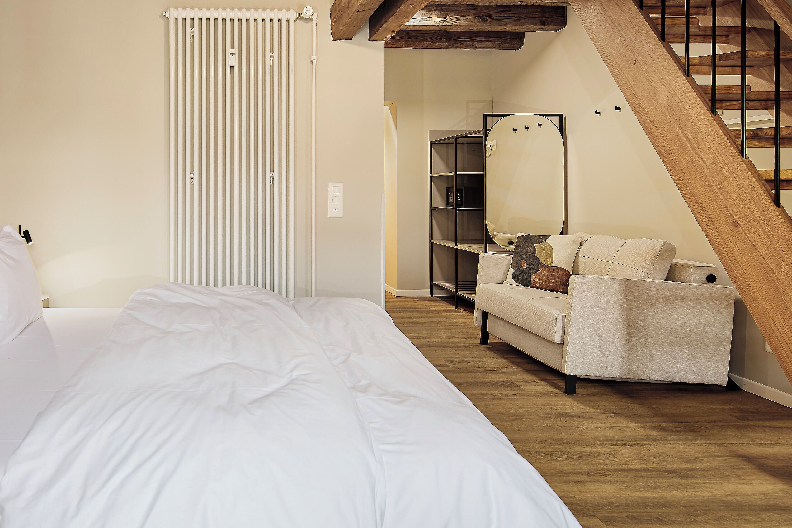 Un dormitorio con cama, sofá, escalera de madera y radiador.