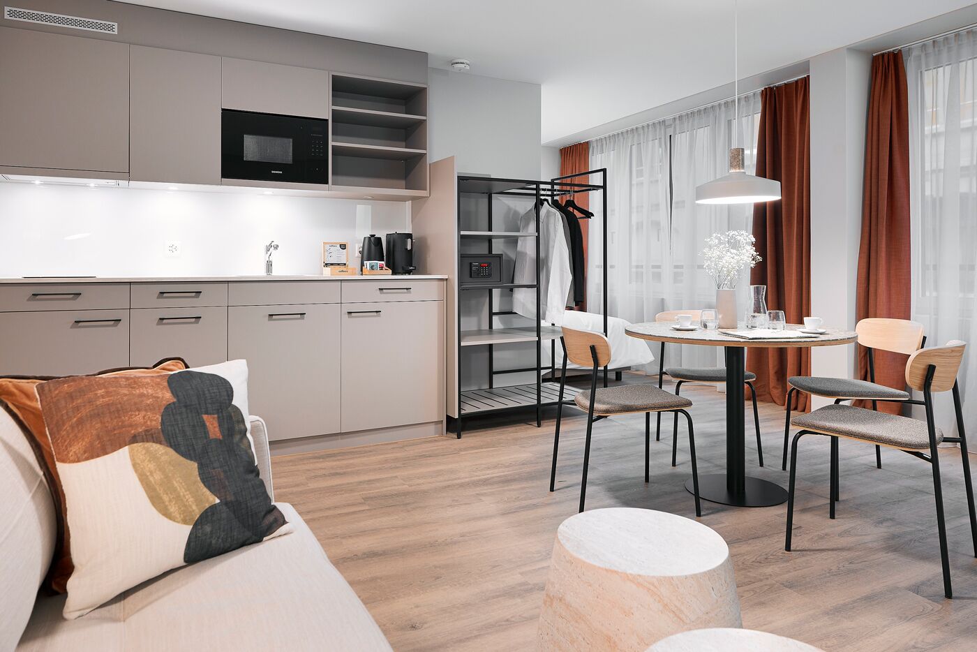 A modern kitchen with a microwave, coffee machine, and cabinets. There is a dining area with a table, chairs, and a vase with flowers.