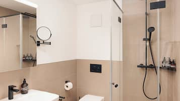 Un baño moderno con ducha envuelta en vidrio, un lavamanos blanco y un inodoro.