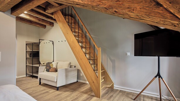 A room with a wooden staircase, a bed, a sofa, a mirror, and a tripod-mounted television. - Stay Sunday (Zürich)