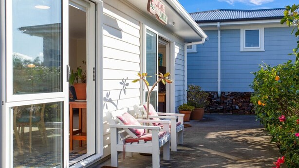 A house with a porch featuring white chairs and potted plants. - The Peninsula Riverside Abode with Garden Views (Auckland West)