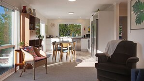 A modern kitchen with a dining area, a large window, and a cozy seating area. - The Peninsula Riverside Abode with Garden Views (Auckland West)
