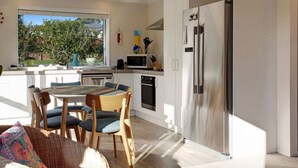 A modern kitchen with white cabinets, a stainless steel refrigerator, and a dining area with a table and chairs. - The Peninsula Riverside Abode with Garden Views (Auckland West)