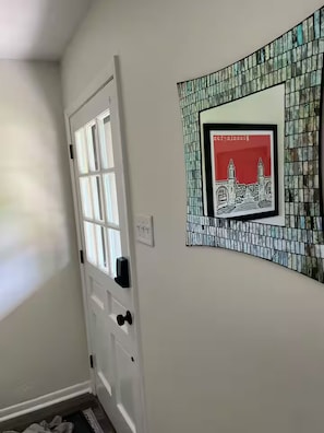 A hallway with a white door, a framed picture of a building, and a tiled wall.