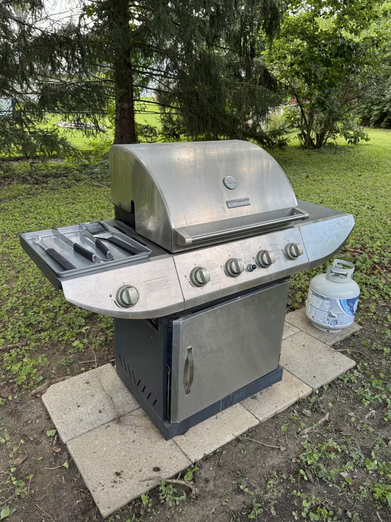 A stainless steel outdoor grill with four burners, a side burner, and a built-in thermometer.