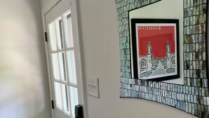 A hallway with a white door, a framed picture of a building, and a tiled wall. - Stadium Stroll Main Level | Walk to Football | Sleeps 8 · 2 BR · 1 Bath (Bloomington)