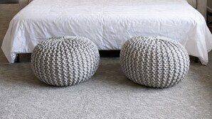 Una camera da letto con un letto grande, due pouf coordinati, un quadro appeso al muro e una porta sulla destra.