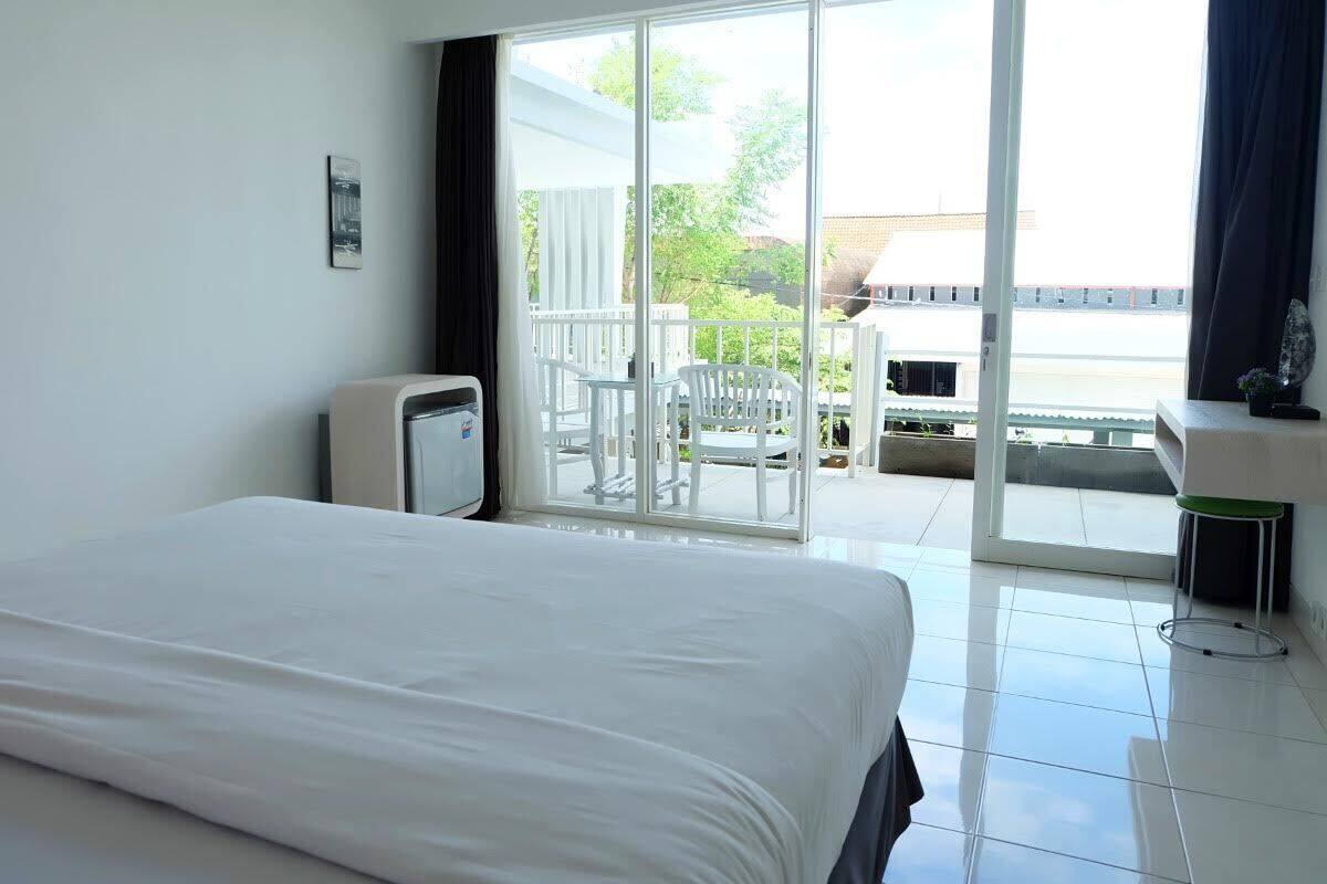 A hotel room with a large bed, a window with a view of the outside, a small table, and a chair.