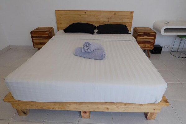 Una cama con estructura de madera, dos mesitas de noche, almohadas negras y una toalla enrollada sobre la cama.