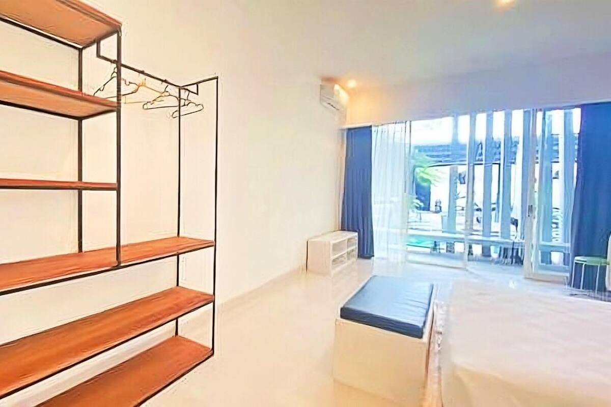 A modern bedroom with a large bed, a wooden shelving unit, and a view of the outdoors through large windows.