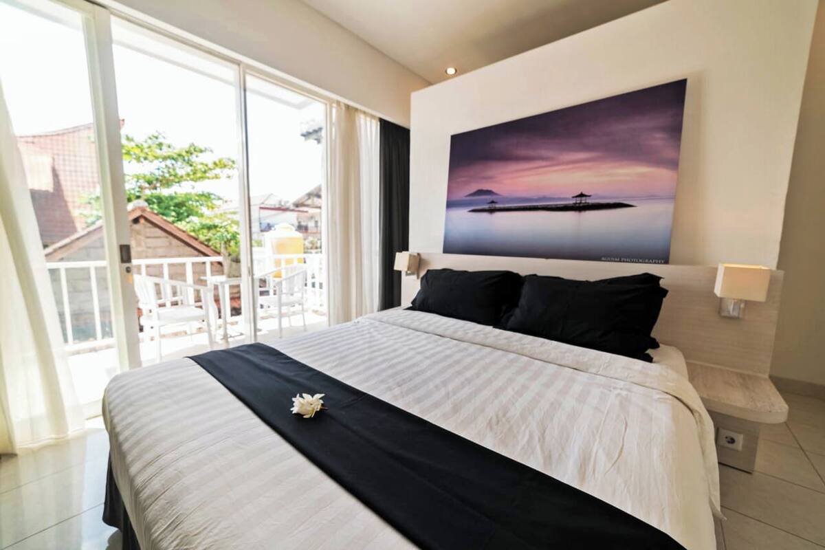 A hotel room with a large bed, a view of the outside, and a painting on the wall.