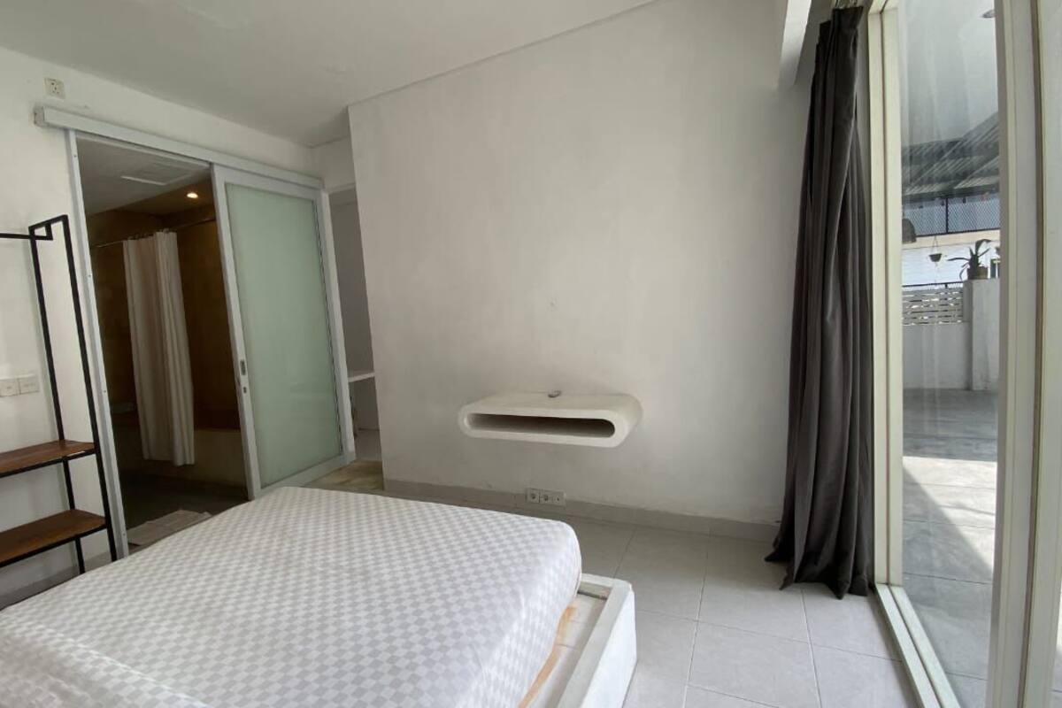 A bedroom with a bed, a wardrobe, a small shelf, and a window with curtains.