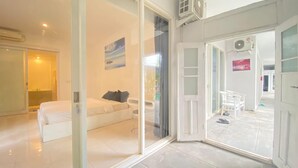 A modern hotel room with a white bed, a sofa, and a glass door leading to a balcony. - Pom Pom's Bali Apartments (Keroboken Kelod)