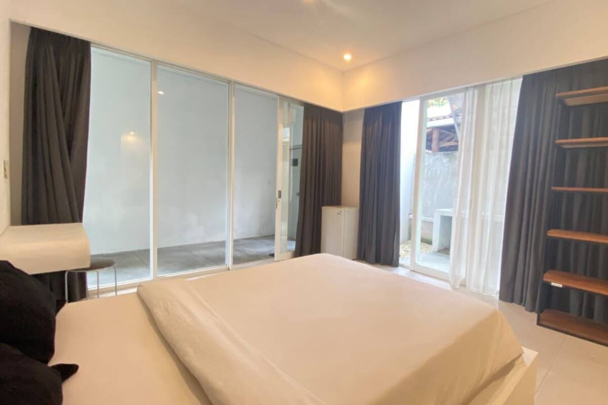 A bedroom with a large bed, sliding glass doors to a balcony, and a built-in shelf unit.