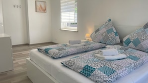 A neatly made bed with patterned pillows and a rolled towel, a bedside lamp, and a window with blinds. - Vacation home Holunder - 7 min. walk to the bathing lake Waldsee Rieden (Rieden)