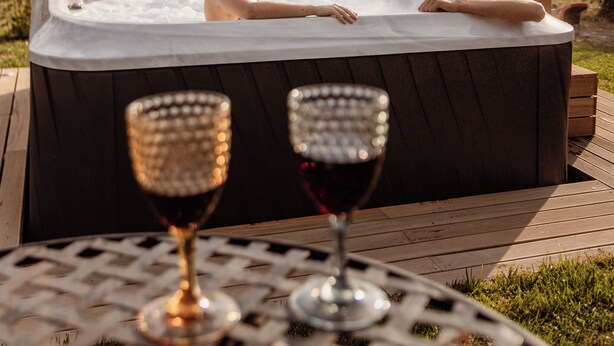 Two people in a hot tub with a table and wine glasses in the foreground.