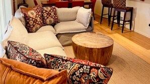 A living room with a sectional sofa, a round wooden coffee table, and a dining area with a table and chairs. - Lovely 4 Bedroom Adobe Minutes to Plaza & Dog-Friendly (Santa Fe)