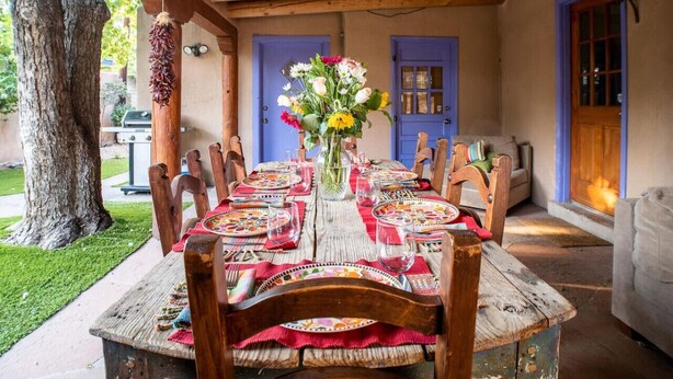 An outdoor dining area with a rustic wooden table set for six, surrounded by wooden chairs. - Lovely 4 Bedroom Adobe Minutes to Plaza & Dog-Friendly (Santa Fe)
