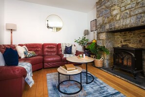 Uma sala de estar acolhedora com um sofá de couro vermelho, um espelho redondo, uma lareira e uma pequena mesa com livros e uma planta.