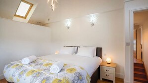 Una camera da letto con un letto, due comodini, un tavolino e una finestra sul tetto, oltre a una scala.