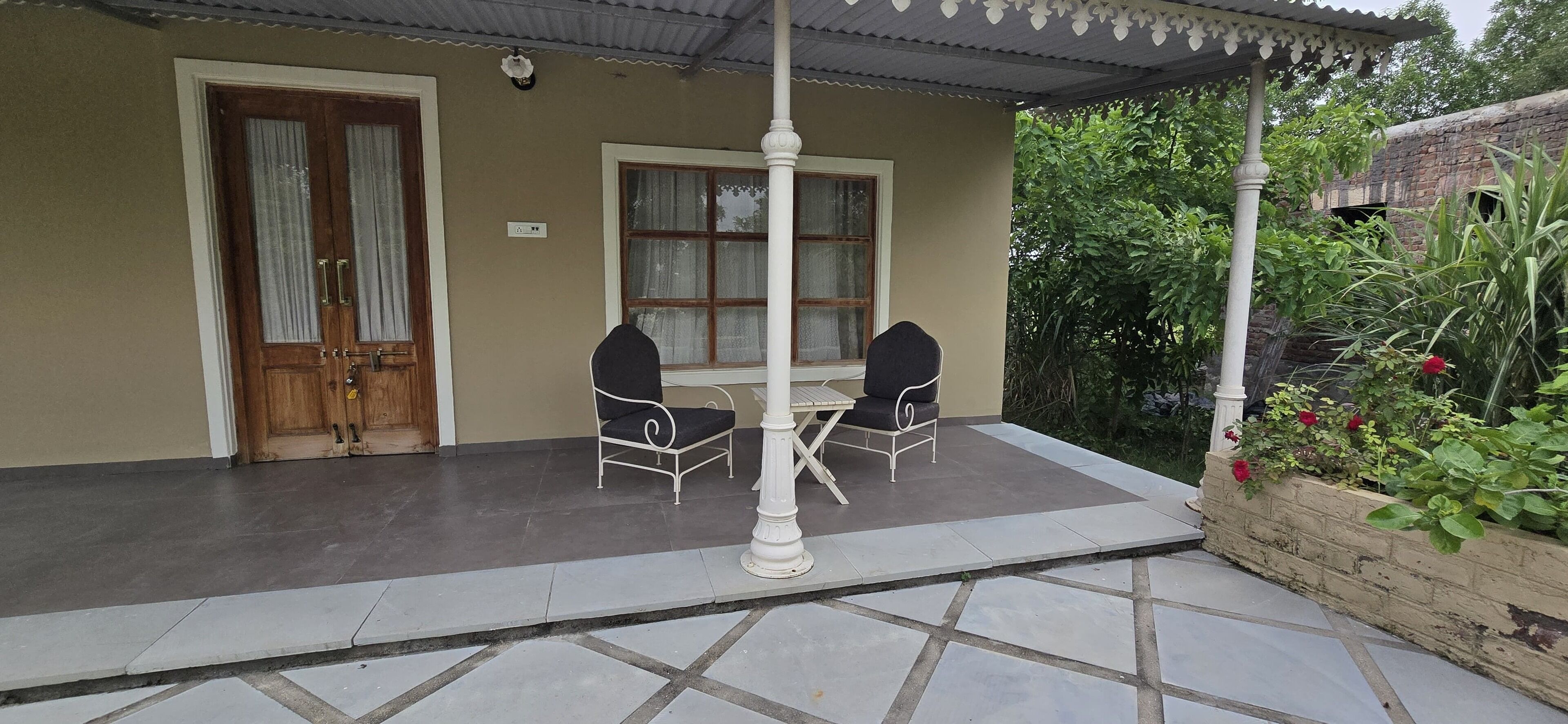 Un patio techado con una mesa, dos sillas, una puerta de madera y una ventana con cortinas.