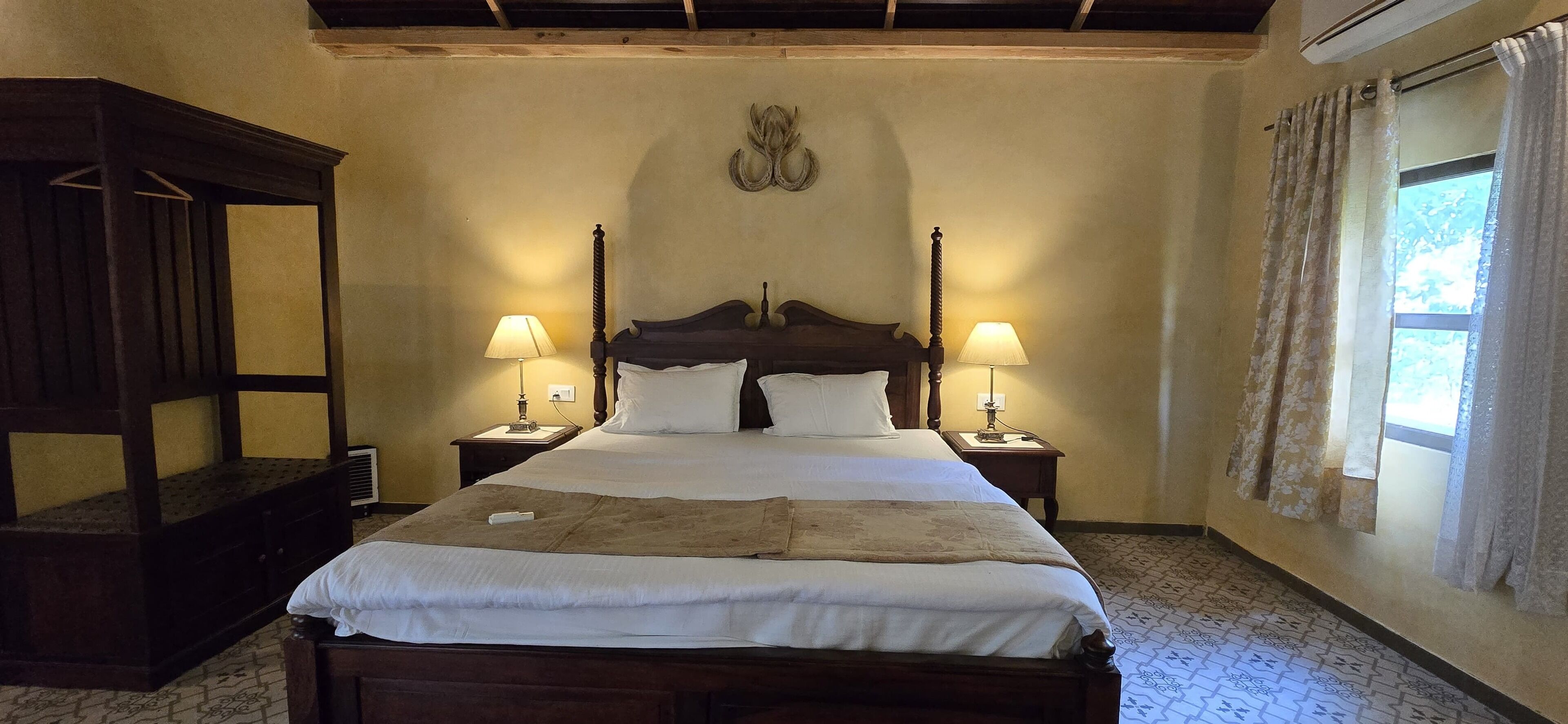 Ein traditionell eingerichtetes Schlafzimmer mit einem großen Bett, zwei Nachttischen mit Lampen, einem Holzschrank und einem Fenster mit Vorhängen.