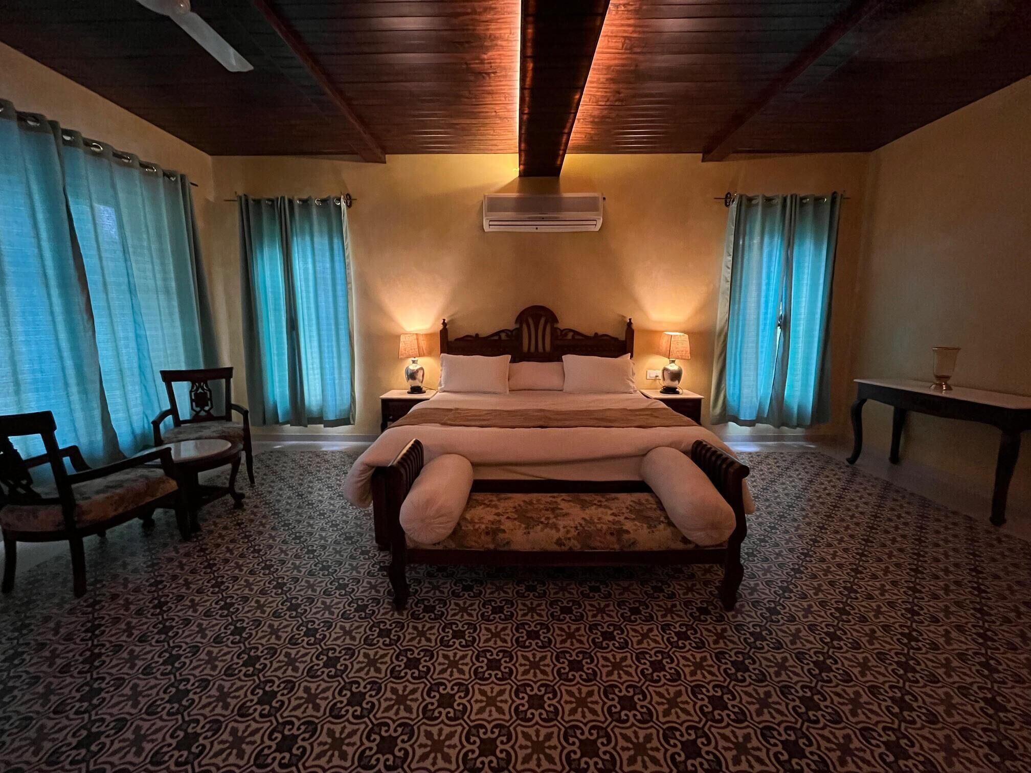 Un letto grande con testiera in legno, due comodini con lampade, una sedia e un tappeto decorato.