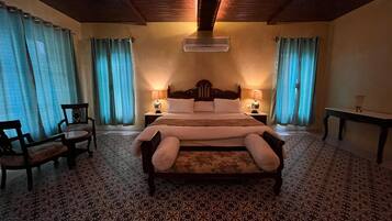 Un letto grande con testiera in legno, due comodini con lampade, una sedia e un tappeto decorato.