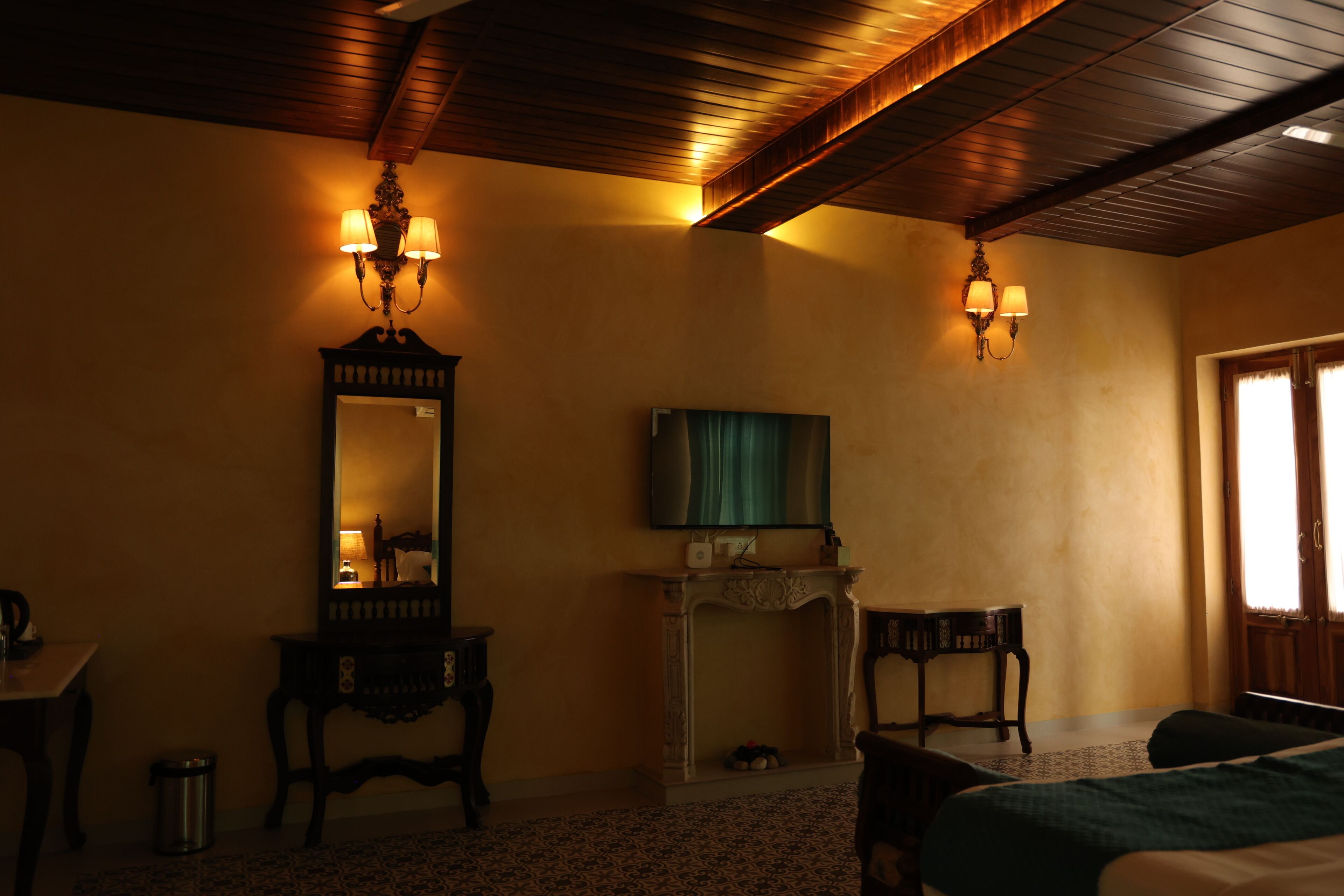 A hotel room with a wooden ceiling, a large mirror, a television, a fireplace, and a bed.